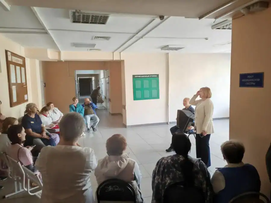 Женщина выступает перед сидящими участниками в больничном коридоре.