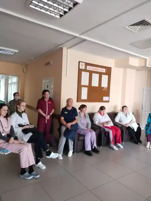 Сотрудники в медицинской одежде и посетители сидят вдоль стены коридора.