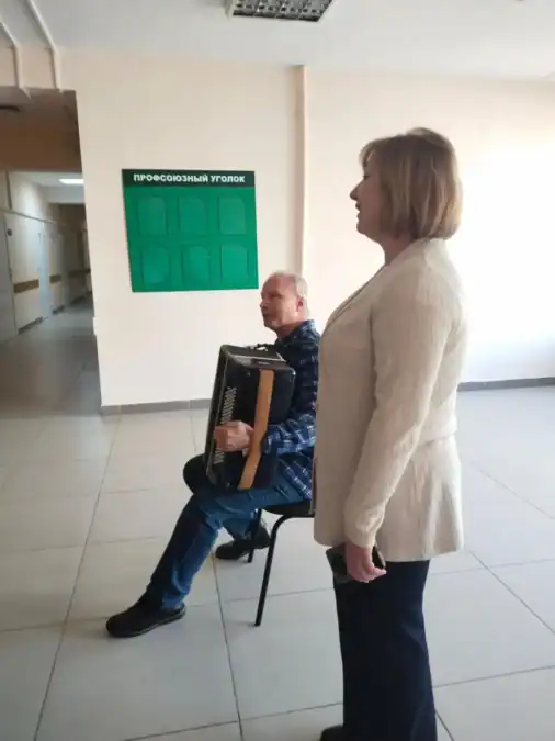Женщина стоит рядом с баянистом в больничном коридоре.