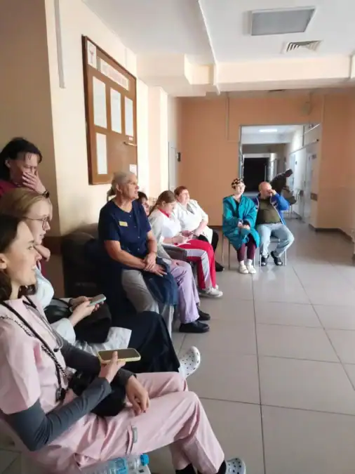 Люди в медицинской одежде и посетители сидят в коридоре.