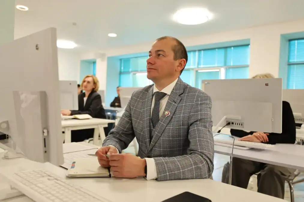 Мужчина в костюме сидит за компьютером и делает записи в блокноте.