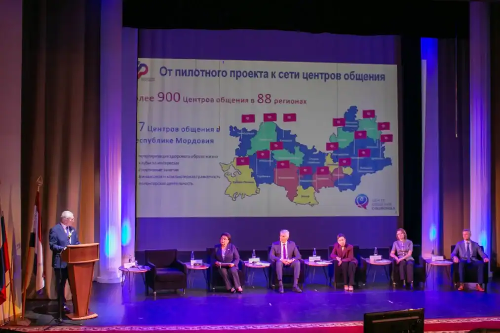 Участники пленарной сессии сидят на сцене перед экраном с картой центров общения.