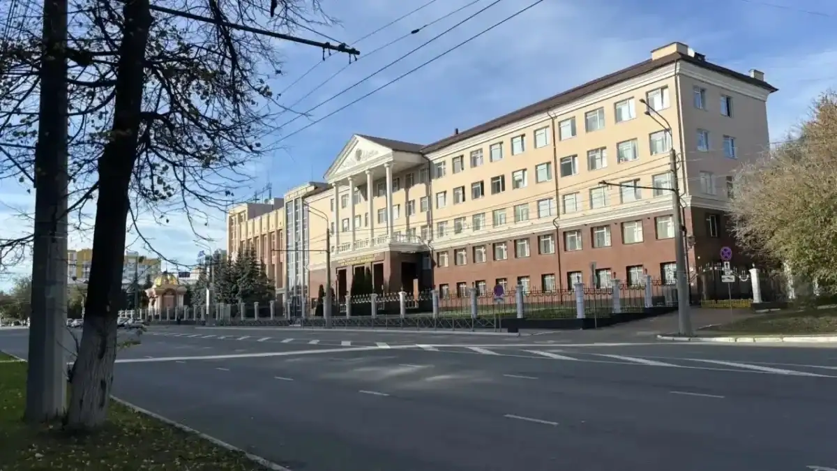 Административное здание за ограждением рядом с широкой городской дорогой.
