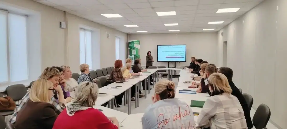 Участники заседания сидят за столами и слушают выступающую у экрана.