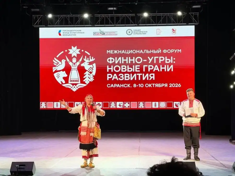 Артисты в национальных костюмах выступают на сцене перед экраном форума.