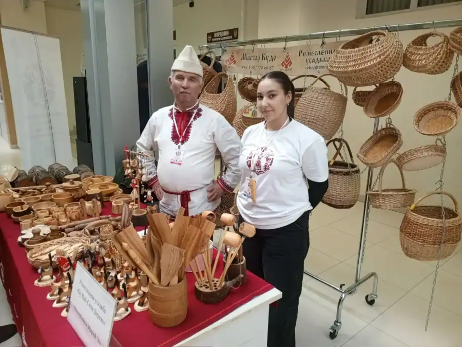 Двое участников у стенда с плетёными корзинами и деревянными изделиями.