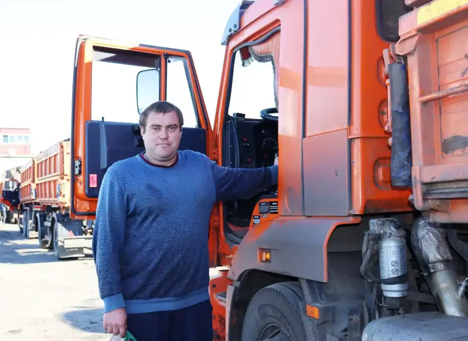 Мужчина стоит у открытой кабины оранжевого грузового автомобиля.