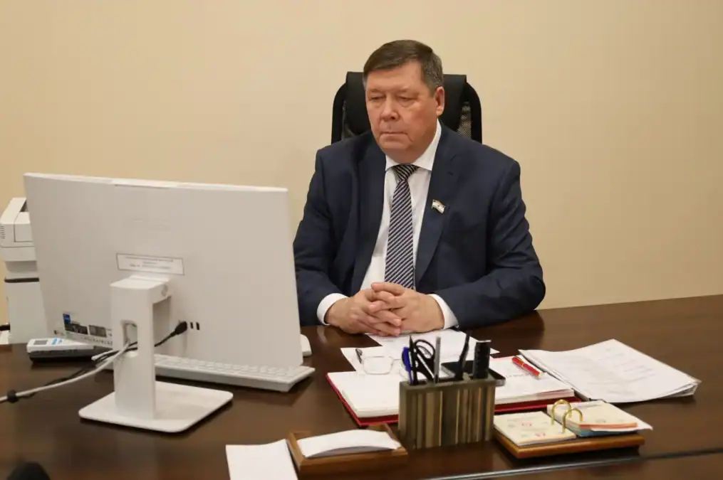 Мужчина в деловом костюме сидит за столом перед монитором и документами.