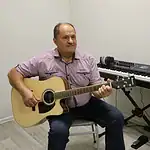 Мужчина играет на акустической гитаре рядом с электронным синтезатором.