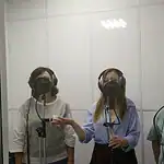 Три женщины в наушниках поют у микрофонов в звукозаписывающей кабине.