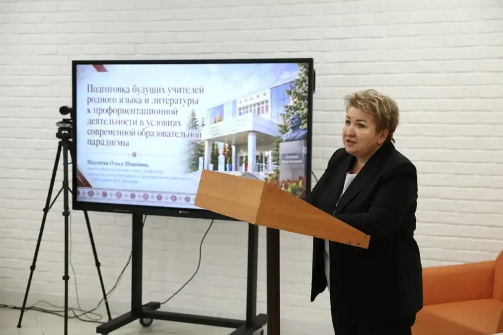 Докладчица выступает у трибуны рядом с экраном презентации.
