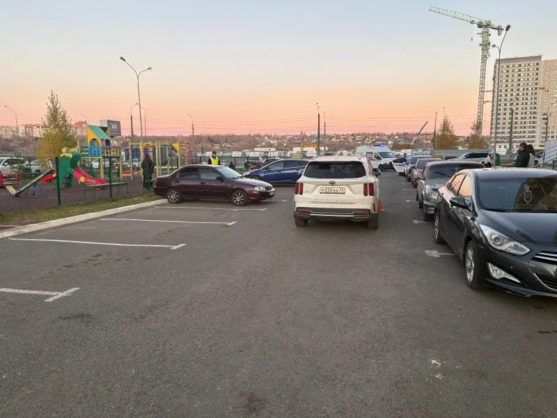 Автомобили стоят во дворовом проезде рядом с детской площадкой и жилыми домами.