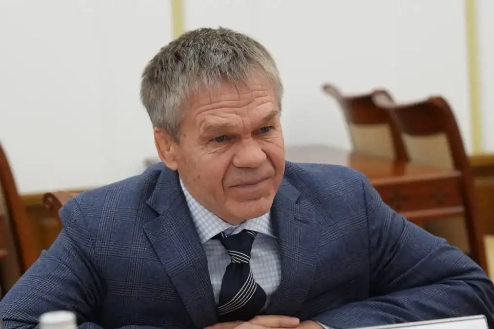 Мужчина в синем пиджаке сидит за столом в помещении.