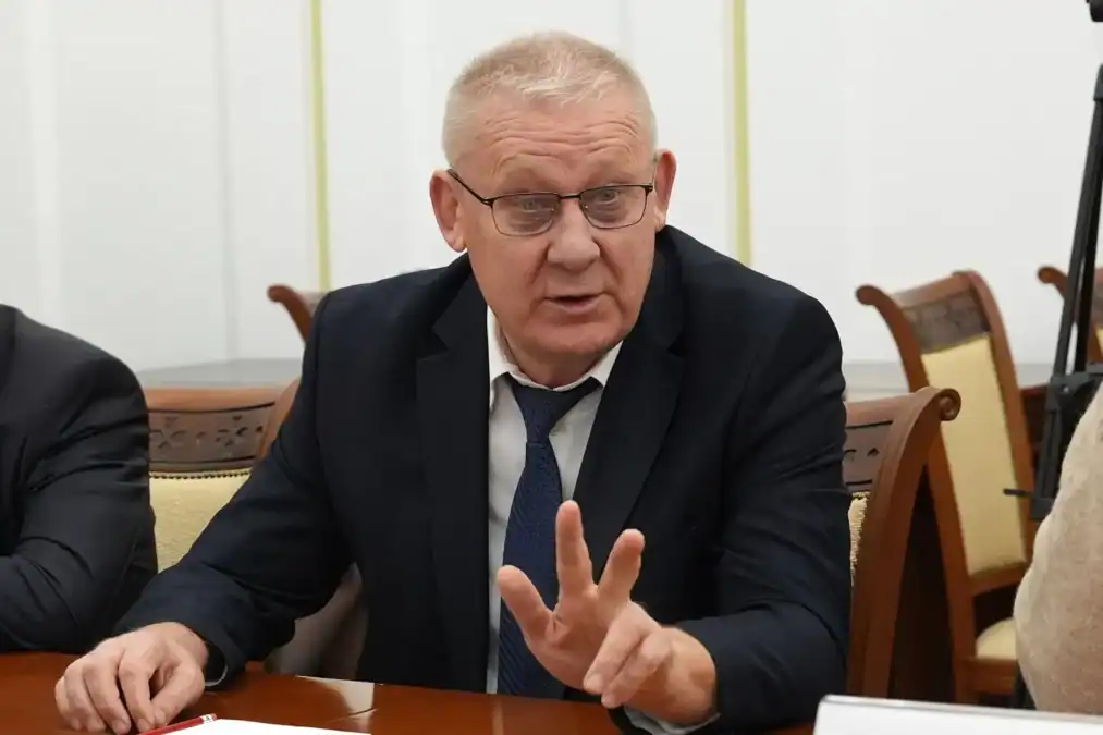 Мужчина в очках жестом показывает два пальца за столом.