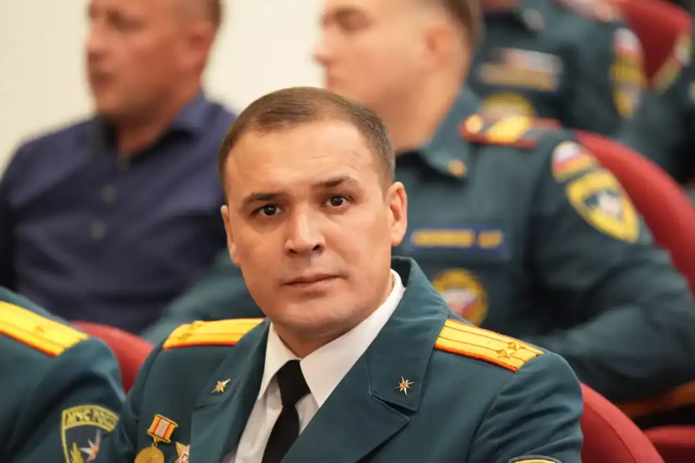 Сотрудник МЧС в парадной форме сидит среди участников мероприятия.