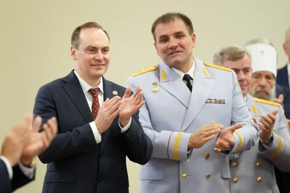 Мужчины в гражданском костюме и парадной форме аплодируют в зале.