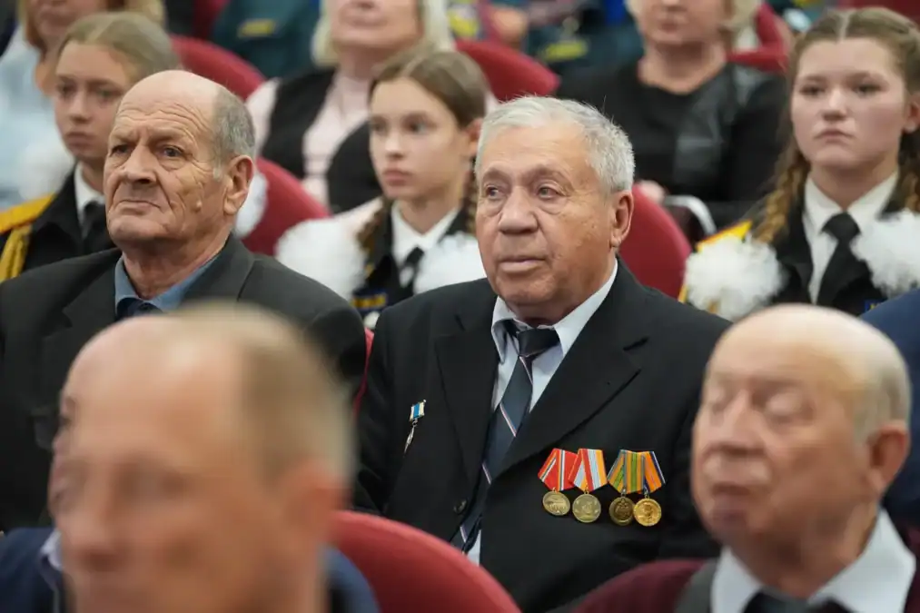 Ветераны с медалями сидят в зрительном зале рядом с молодёжью.