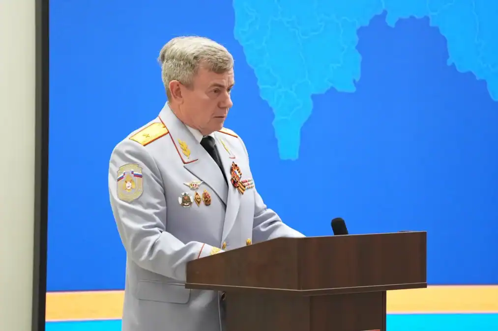 Офицер в светлой парадной форме выступает с трибуны перед экраном.