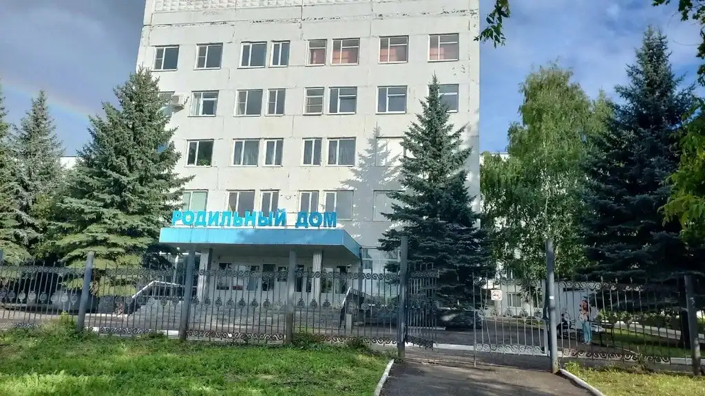 Вход в многоэтажное здание родильного дома за металлическим ограждением.