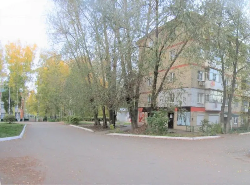 Двор у пятиэтажного жилого дома с деревьями и тротуаром.