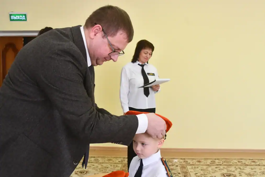 Мужчина надевает оранжевый берет ребёнку в кадетской форме.