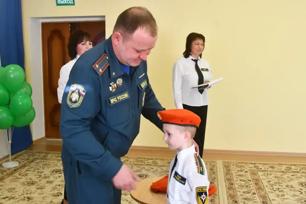 Сотрудник МЧС поправляет форму мальчику в оранжевом берете.
