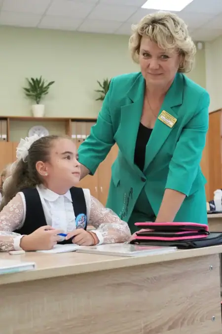 Учительница стоит рядом с ученицей, сидящей за партой.
