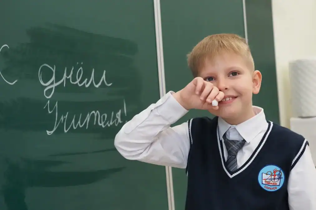 Школьник у доски держит мел рядом с надписью ко Дню учителя.