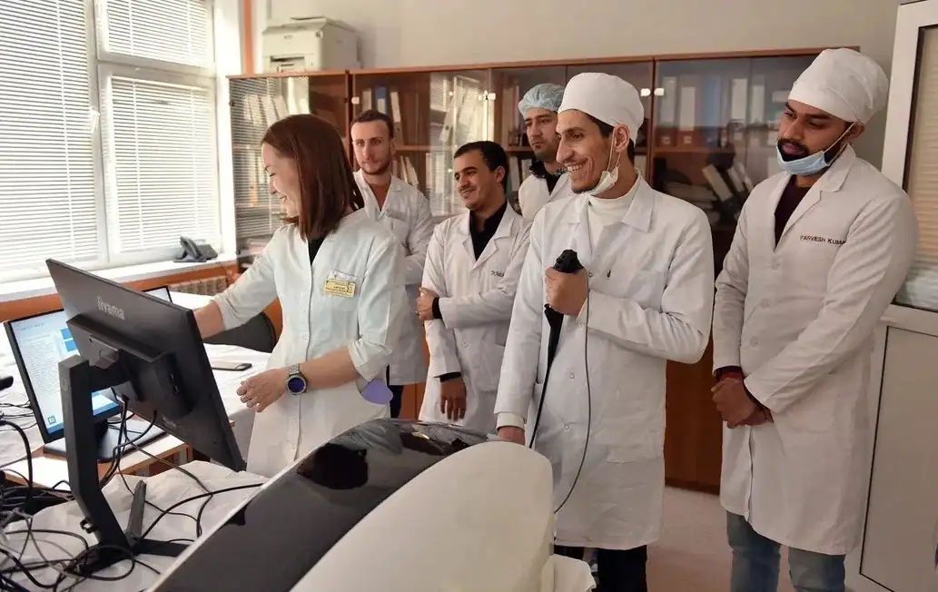 Студенты в белых халатах наблюдают за работой у медицинского оборудования.