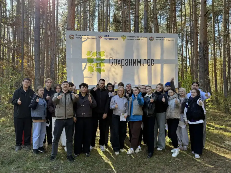Большая группа участников позирует в лесу у баннера «Сохраним лес».