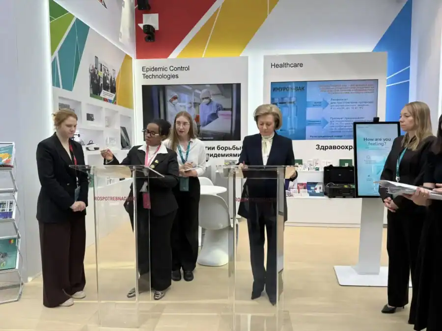Участницы встречи стоят у прозрачных трибун на стенде медицинских технологий.