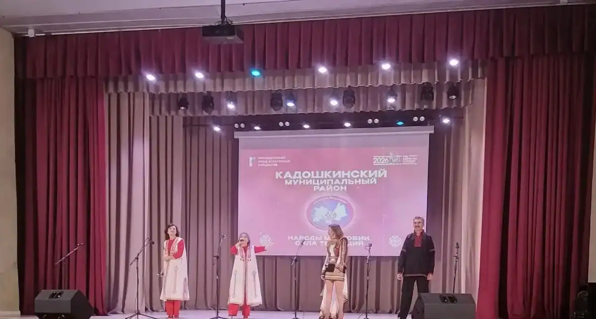 Артисты в народных костюмах стоят на сцене районного Дома культуры.