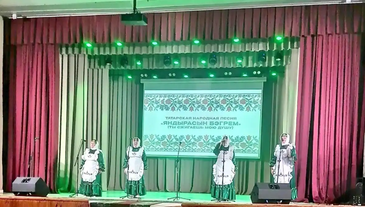 Четыре артистки в национальных костюмах поют у микрофонов на сцене.