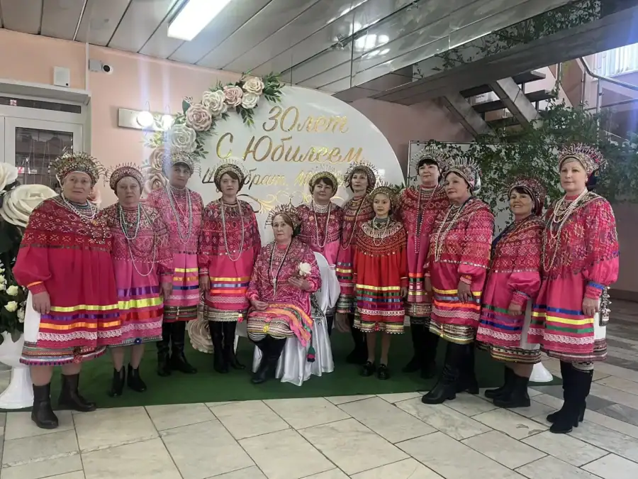 Группа женщин в ярких народных костюмах позирует у декоративной фотозоны.