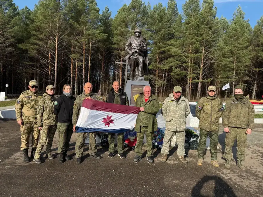 Поисковики с флагом стоят перед памятником советскому солдату.