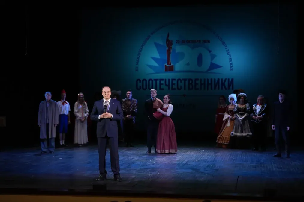 Артисты в костюмах стоят на сцене перед экраном фестиваля «Соотечественники».