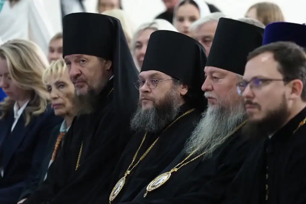 Священнослужители в чёрных облачениях сидят среди участников мероприятия.