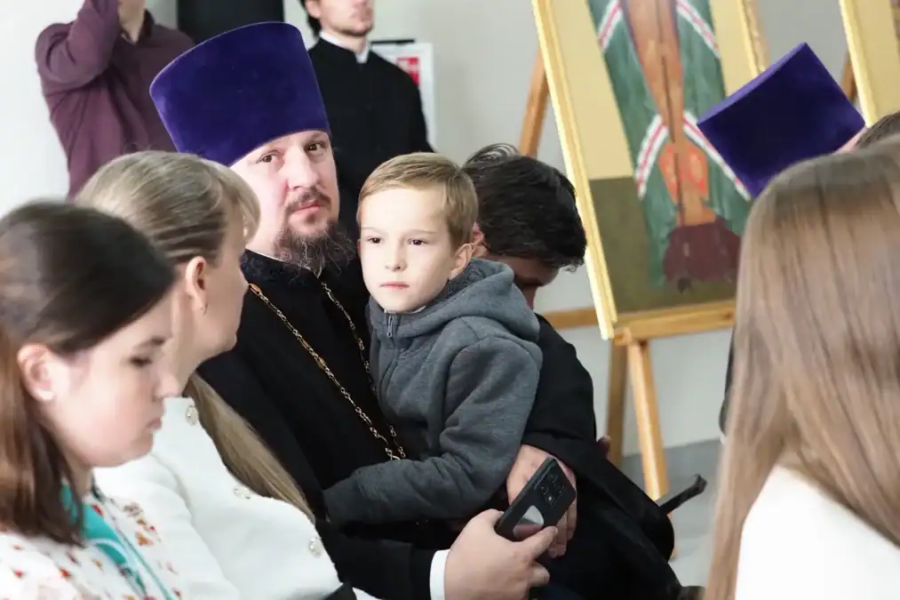 Священнослужитель держит на руках мальчика в зале с иконами.