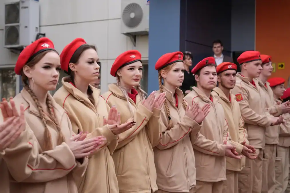 Юнармейцы в бежевой форме и красных беретах аплодируют.