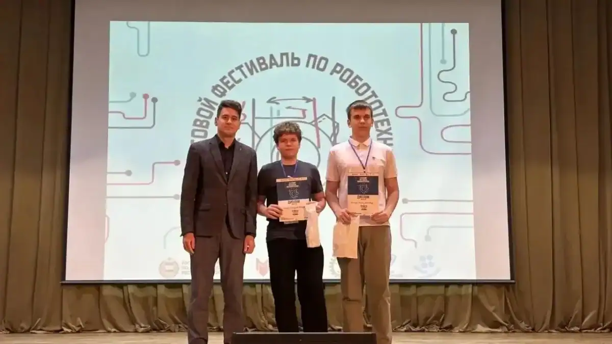 Трое мужчин на сцене держат дипломы на фоне экрана фестиваля.