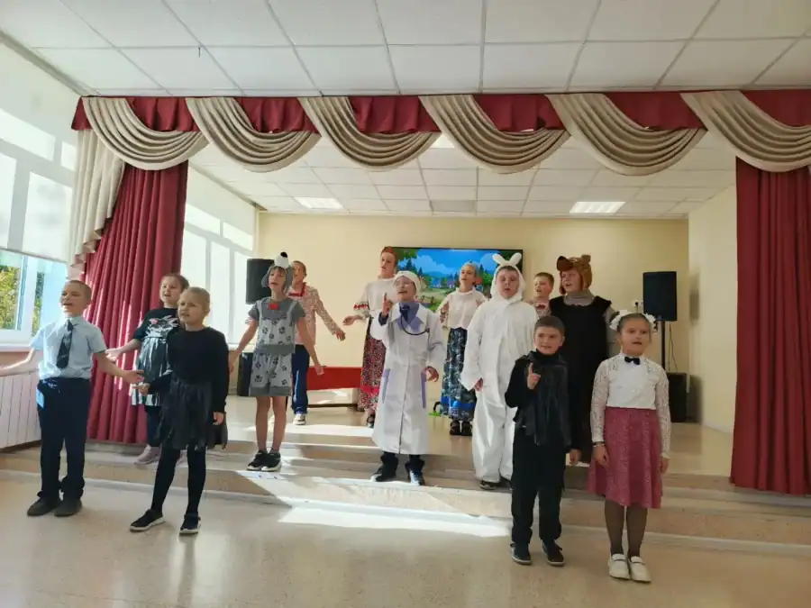 Дети в костюмах исполняют театральный номер на школьной сцене.