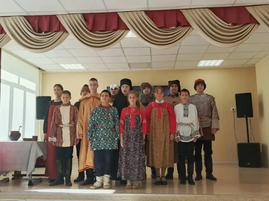 Группа школьников в народных и исторических костюмах стоит на сцене.