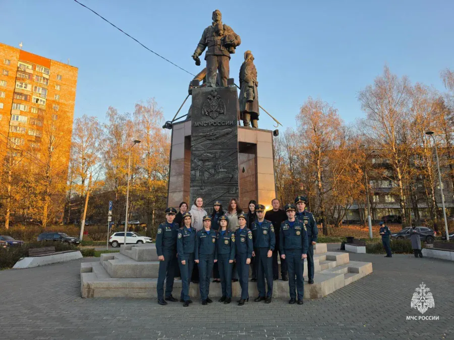 Сотрудники МЧС стоят группой у памятника на городской площади.