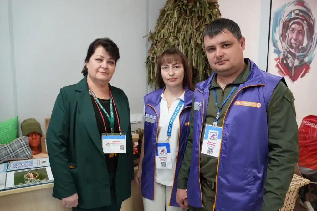 Трое взрослых с бейджами стоят рядом с выставочным стендом.