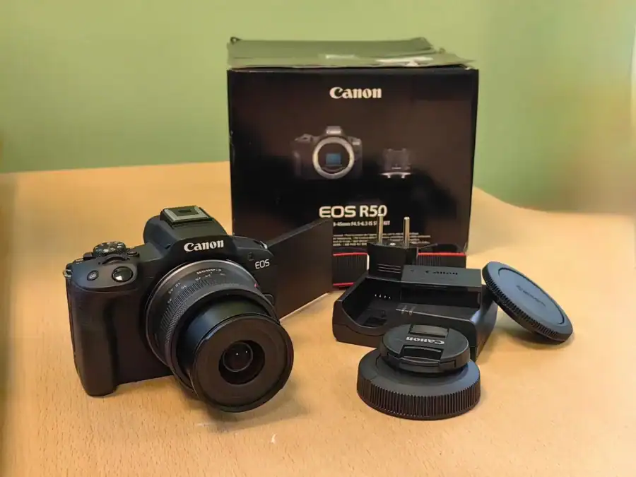 Беззеркальная камера Canon с объективом, упаковкой и комплектующими на столе.