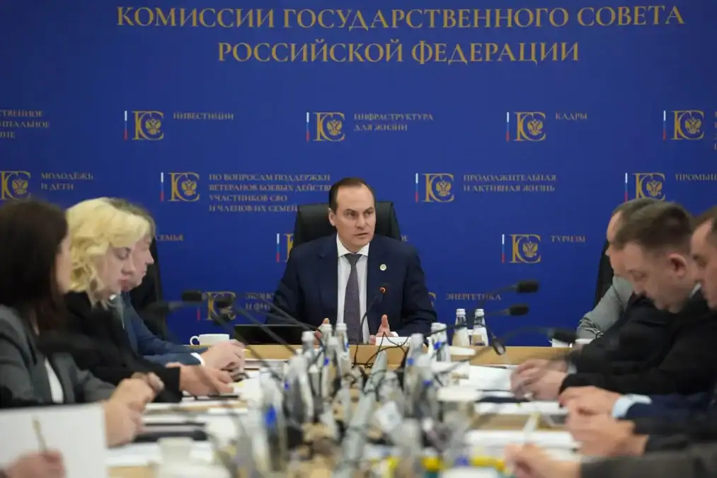 Участники заседания комиссии сидят за столом с микрофонами и документами.