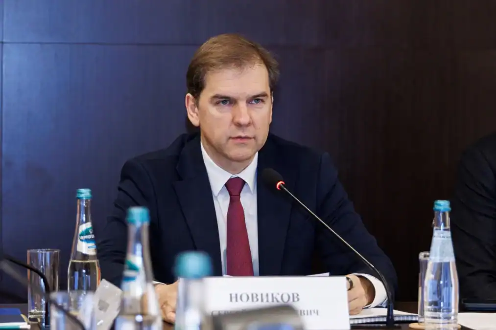 Мужчина в костюме выступает в микрофон за столом заседания.