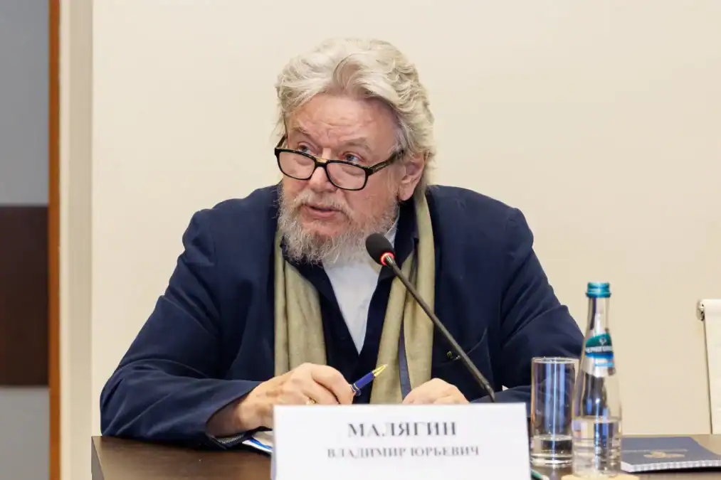 Мужчина в очках говорит в микрофон во время заседания.