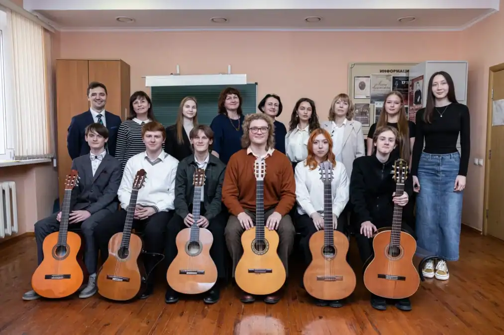 Преподаватели и молодые музыканты позируют в классе с классическими гитарами.