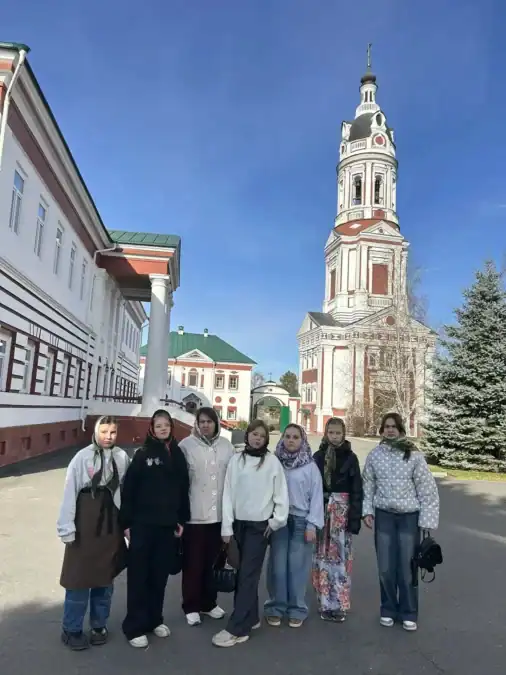 Группа школьниц стоит на территории монастыря рядом с высокой колокольней.